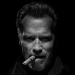 Arnold Schwarzenegger smokes a cigar in the dark
